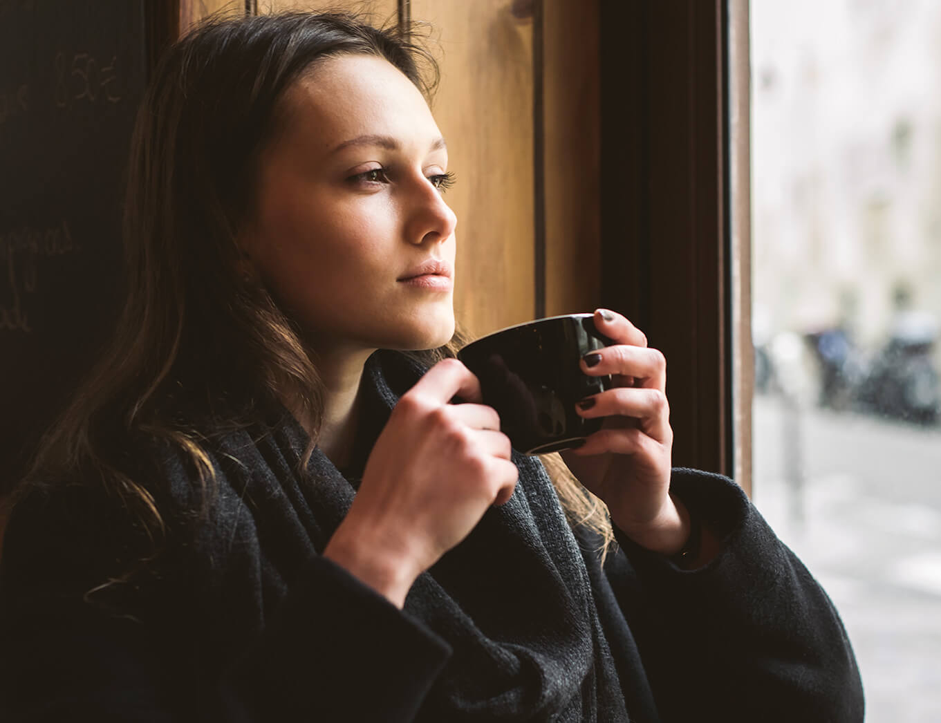woman sitting and looking out the window while holding a cup of tea
