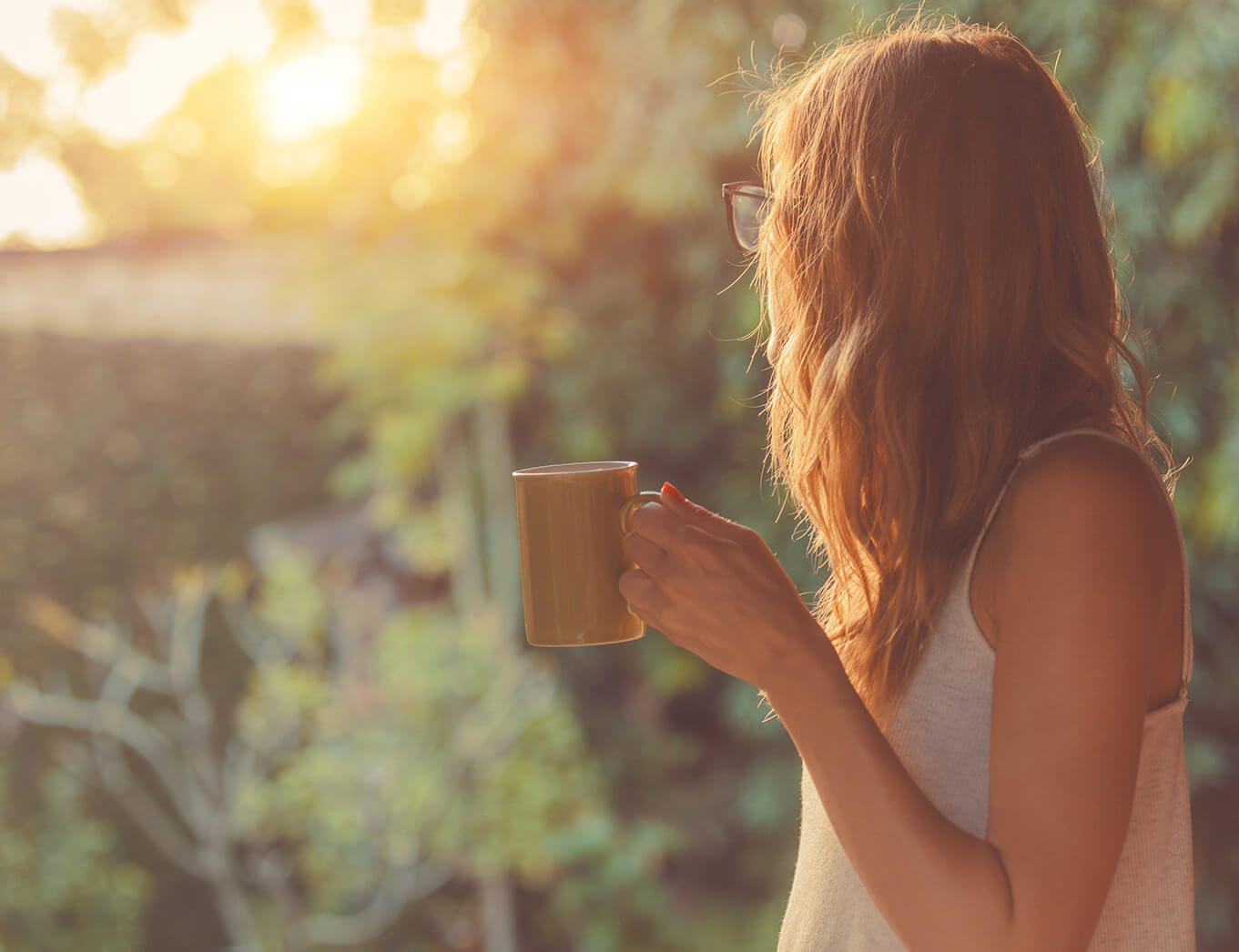 woman with glasses looking away from the camera and holding a cup of tea