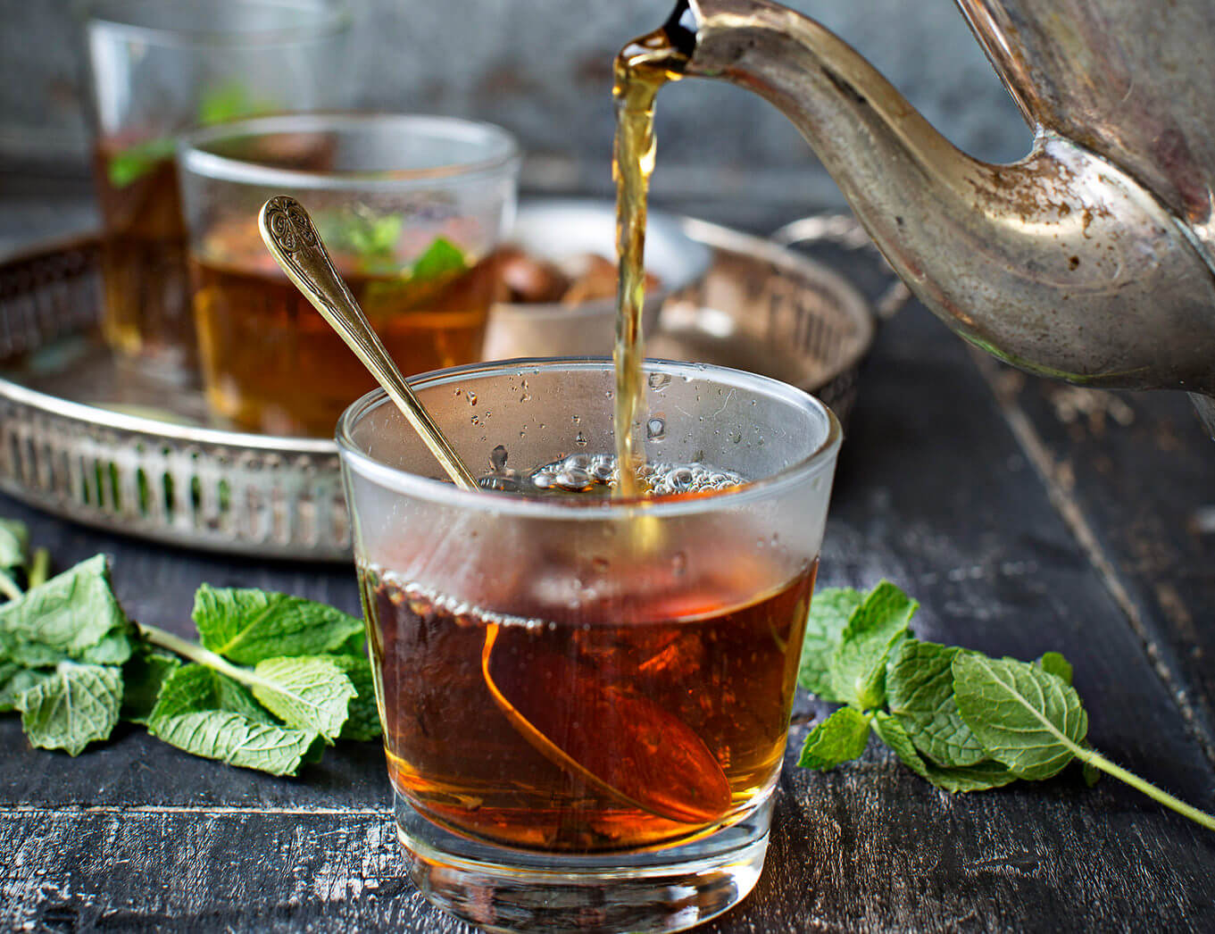 tea being poured from a silver pot into a glass with a spoon in it