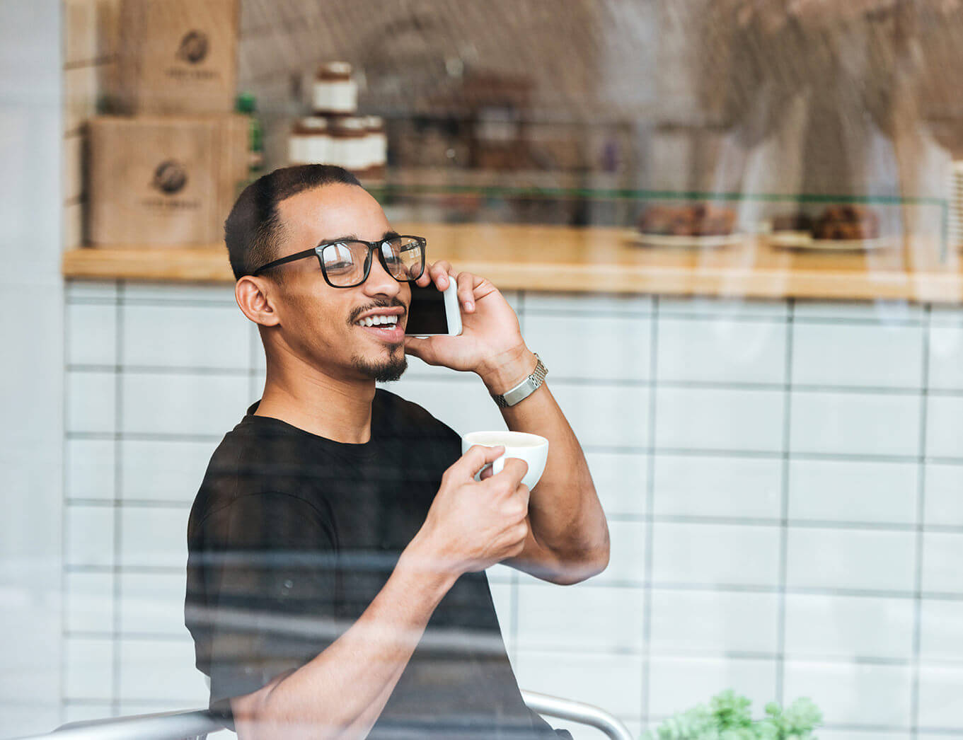 man sitting in a cafe holding a cup of tea and talking on a mobile phone