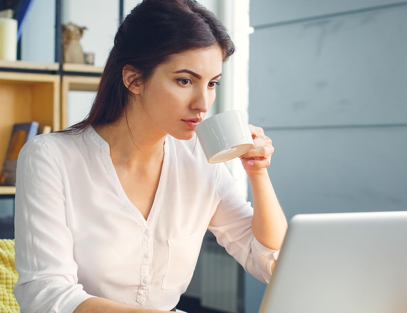 woman taking a sip of tea while working at a laptop