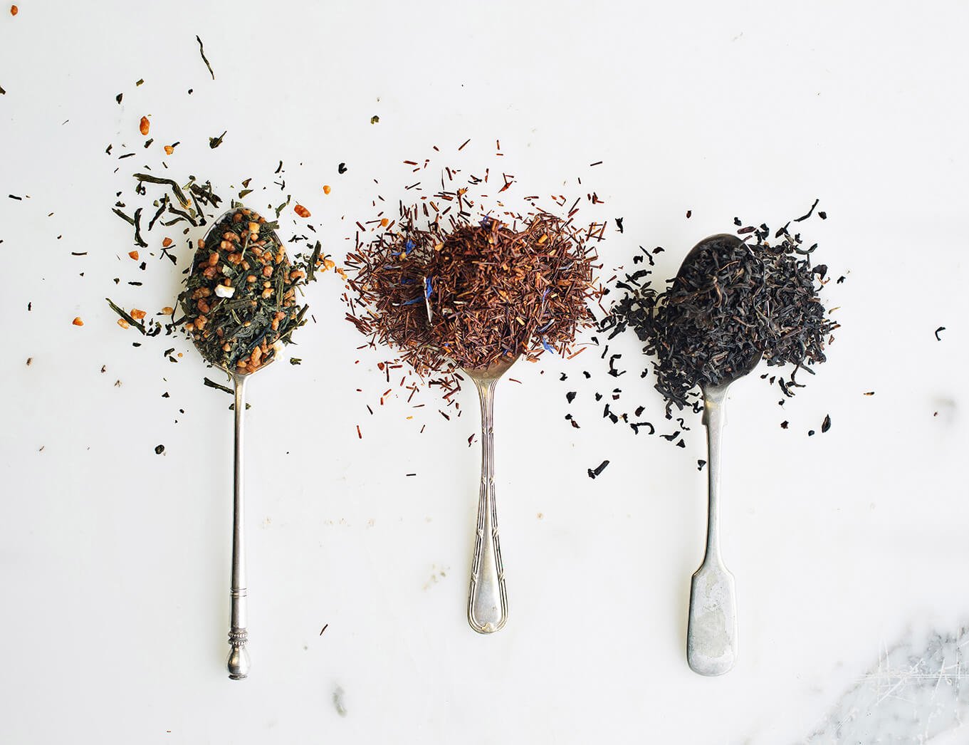three silver spoons lying flat and each holding different tea leaves