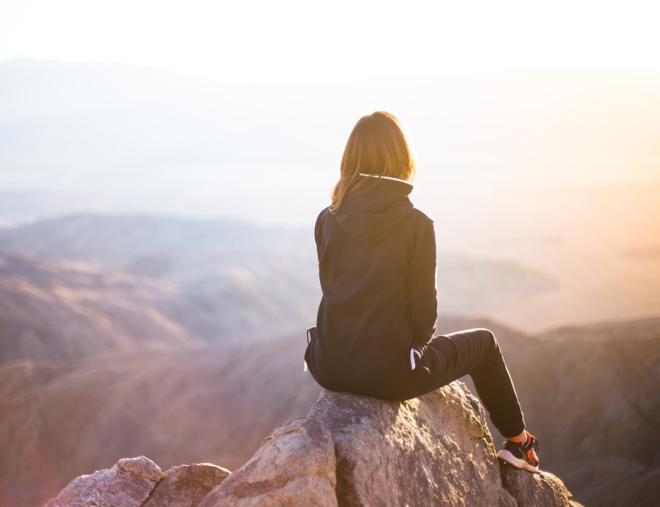 woman siting on a rock looking into the distance over mountains and a sunset
