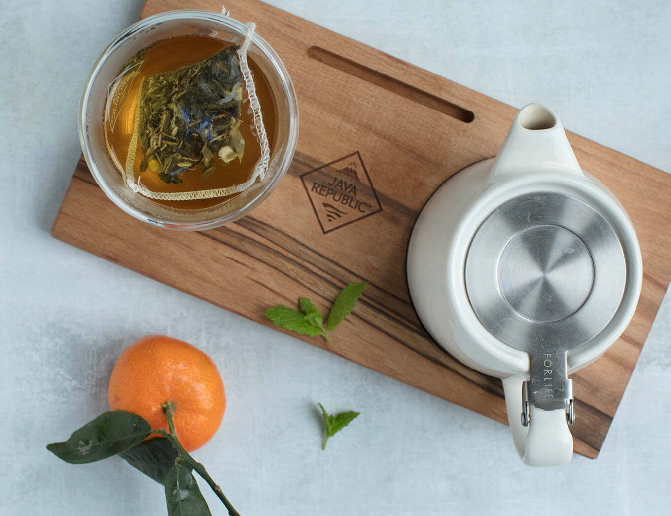 pot of tea next to a glass of tea and an orange