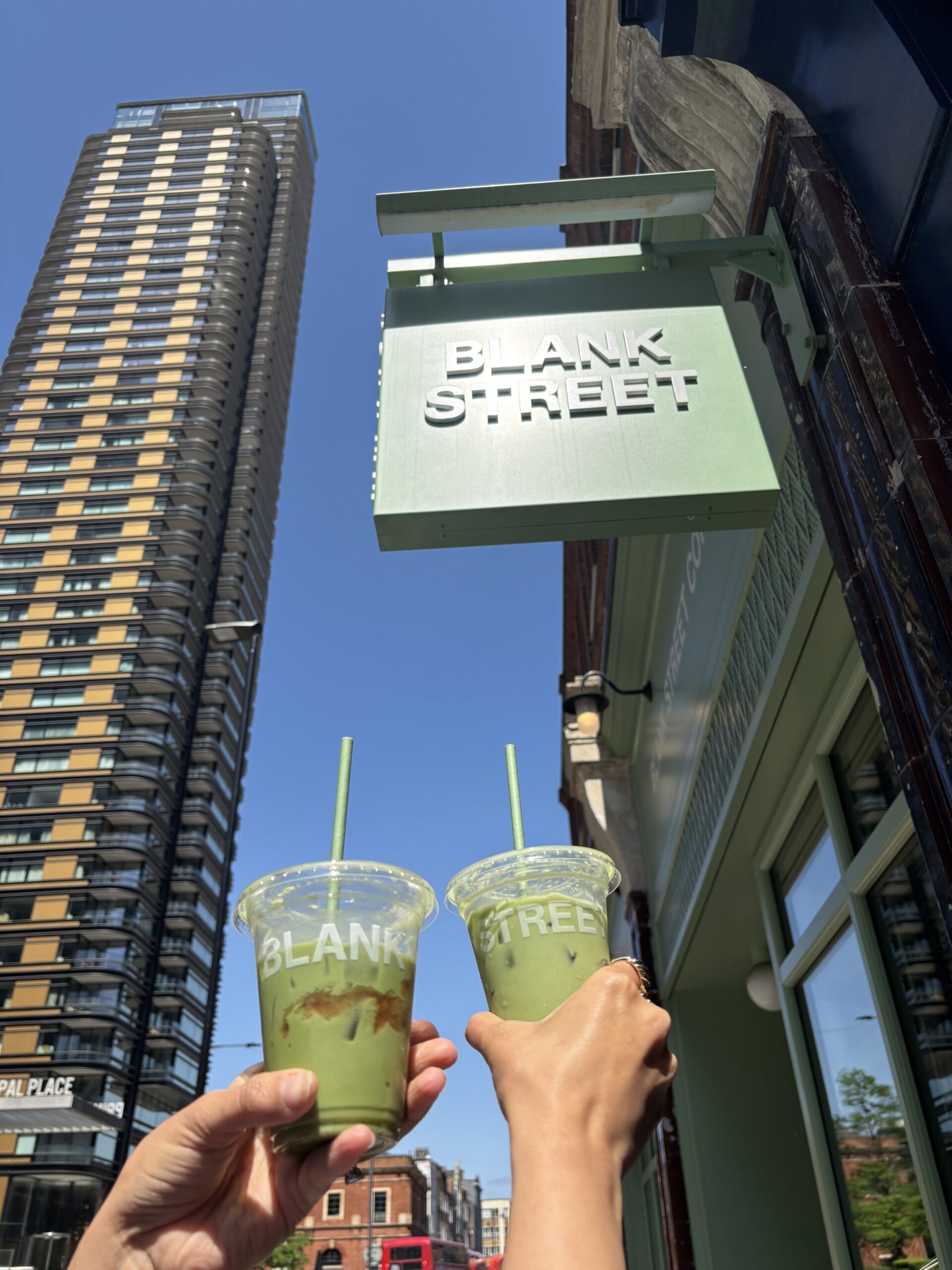 Two hands holding iced matcha drinks outside Blank Street in London